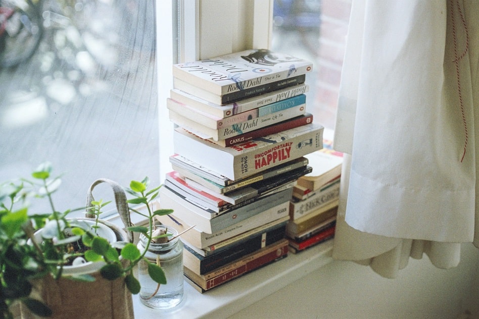 A stack of books sitting on a windowsill