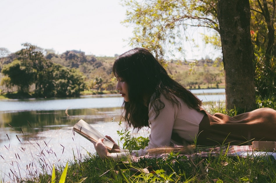 Young women sitting outside reading book on the grass